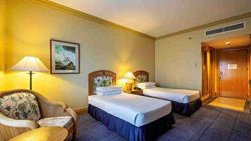 A hotel room with two beds, a chair, a lamp, and a painting on the wall.
