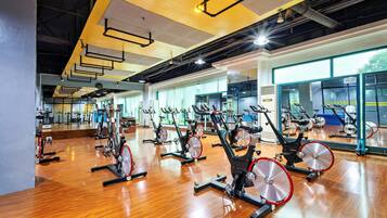 A gym with multiple stationary bikes arranged in rows, large windows, and a wooden floor.