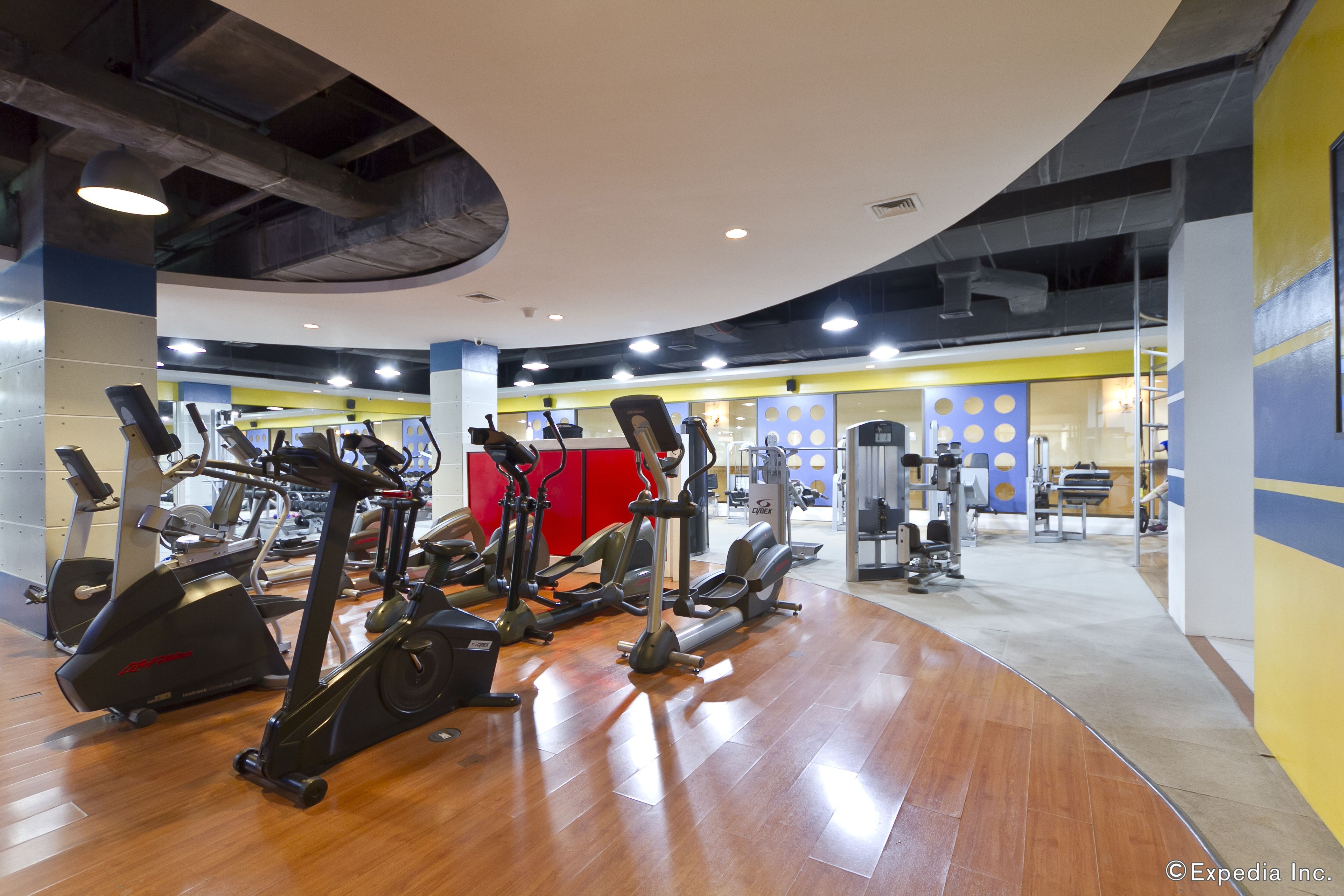 Et fitnesscenter med forskellige konditionsmaskiner, et rødt træningsområde og et styrkeafsnit.