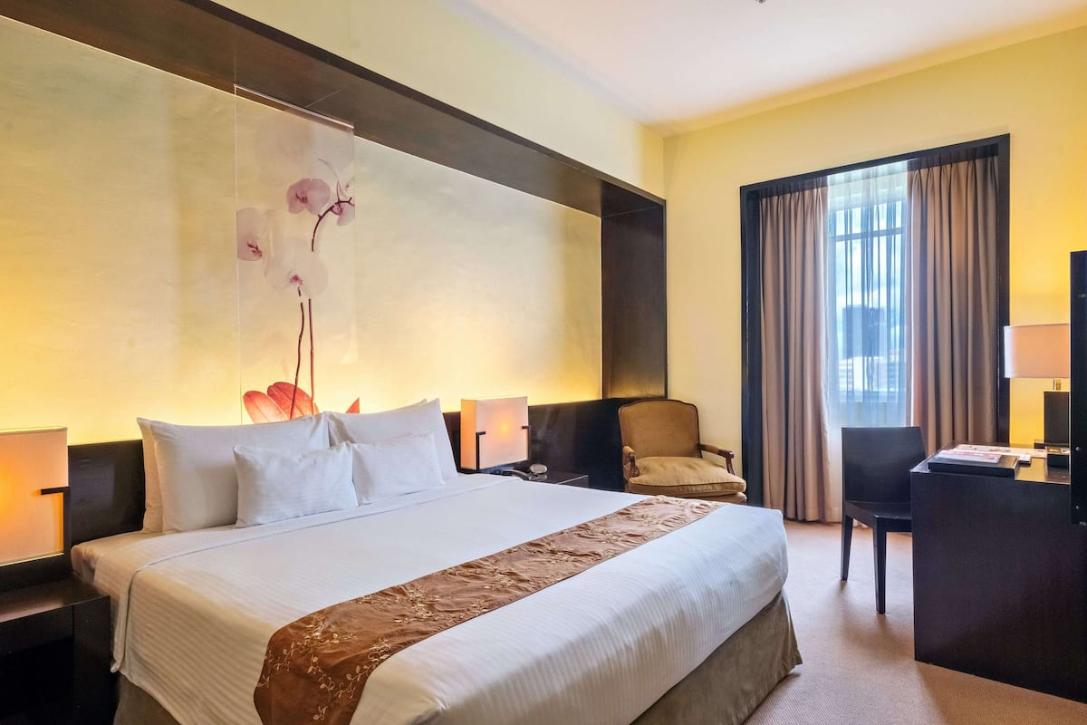 Une chambre d’hôtel avec un grand lit, un bureau, une chaise et une fenêtre avec des rideaux.