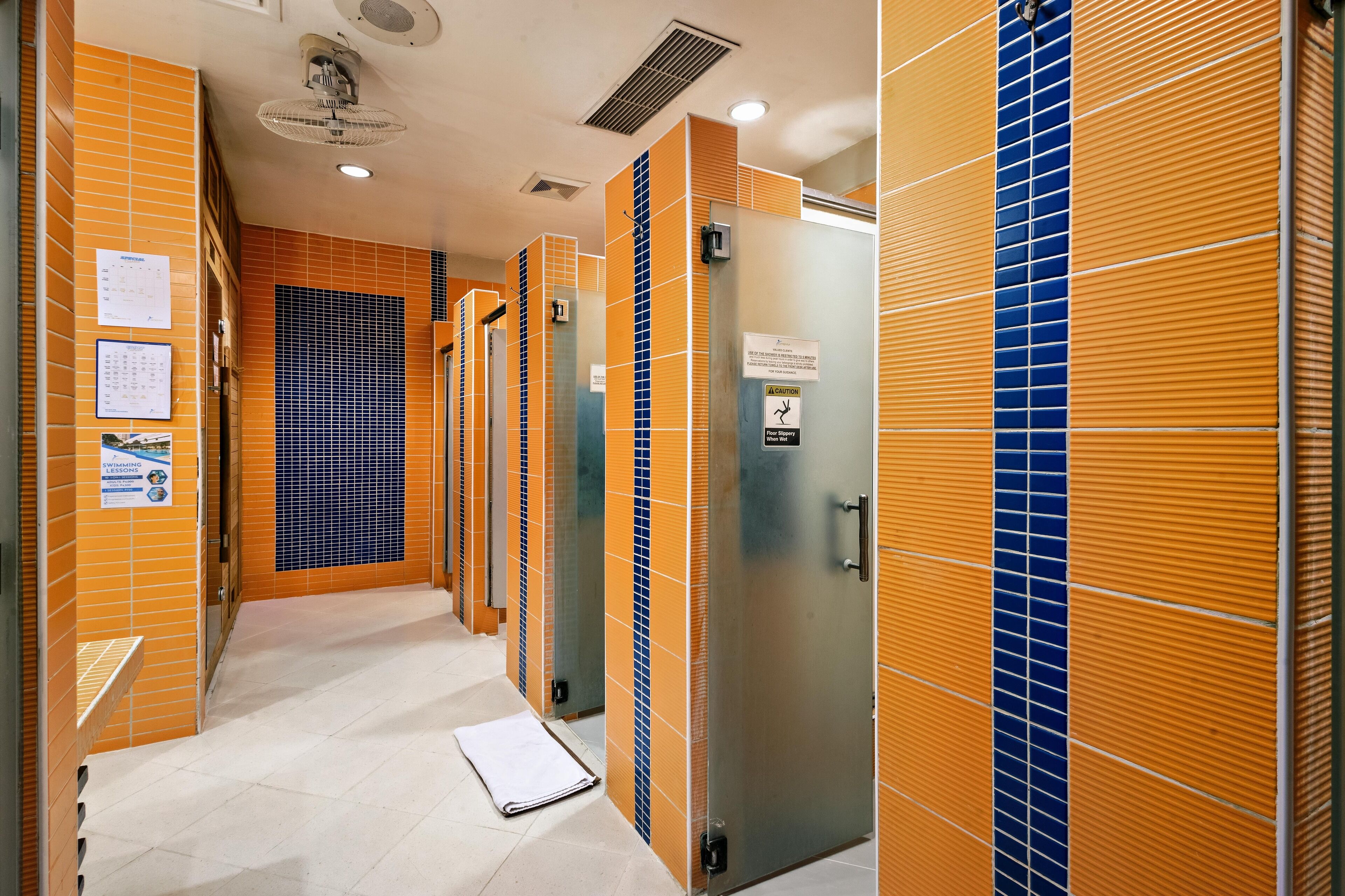 A corridor with tiled walls, a ceiling fan, and a vent.