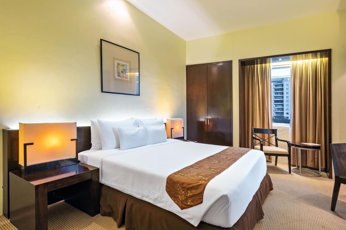 Une chambre d’hôtel avec un grand lit, deux tables de chevet, une chaise, un bureau et une fenêtre avec des rideaux.