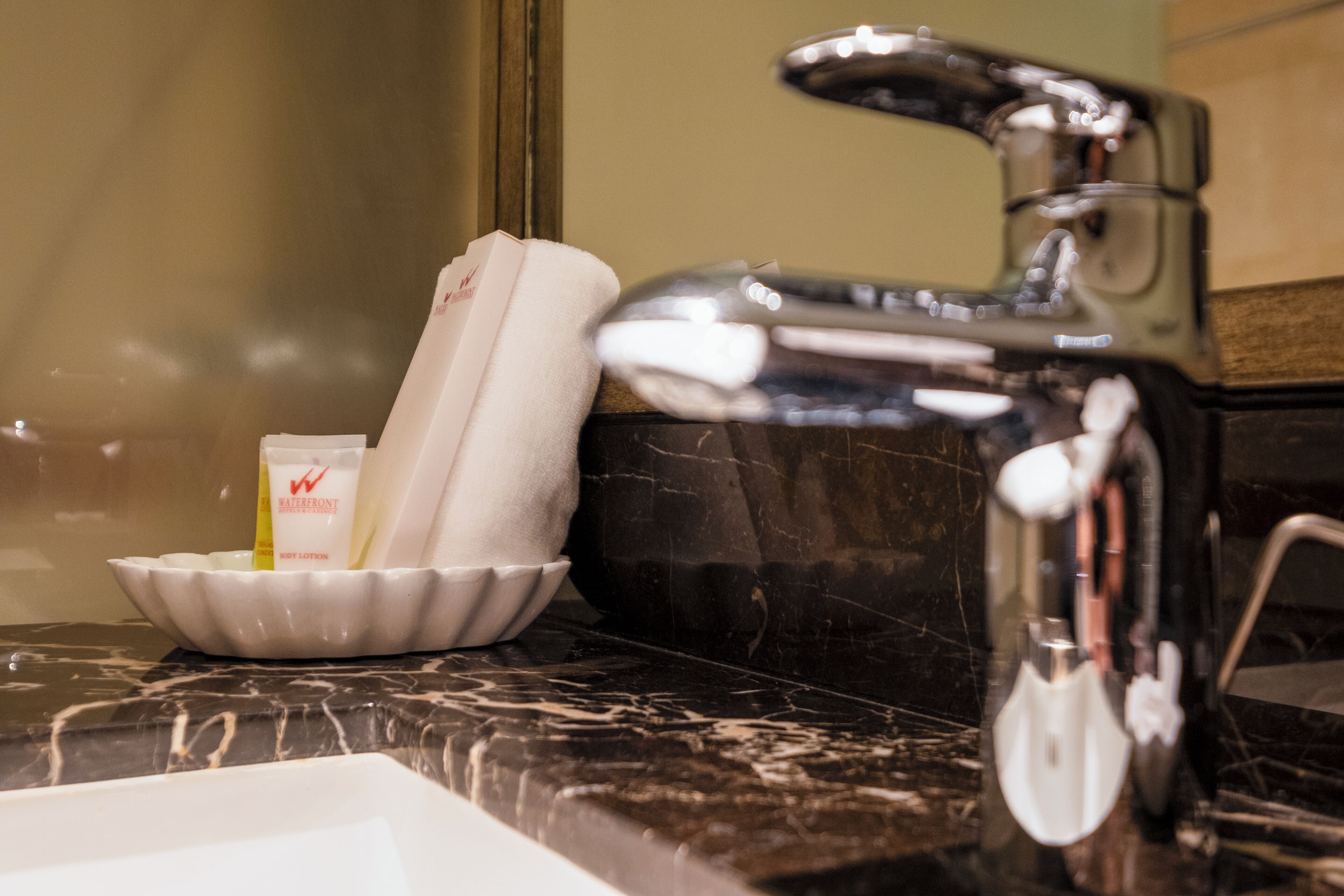 A bathroom sink with a marble countertop, a white soap dish, and a bottle of lotion.