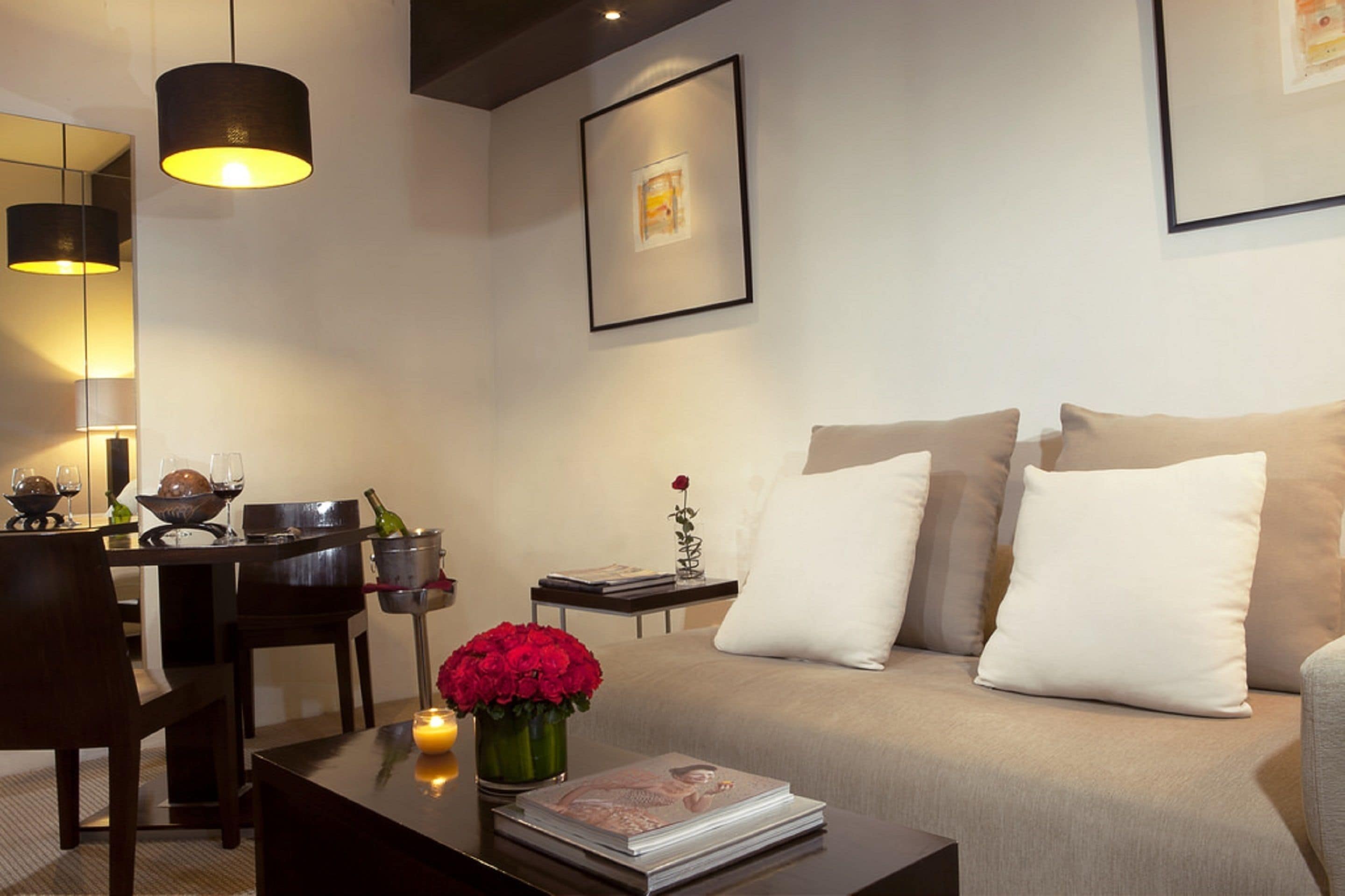 A modern living room with a sofa, a coffee table with a magazine, a vase of red flowers, and a framed picture on the wall.