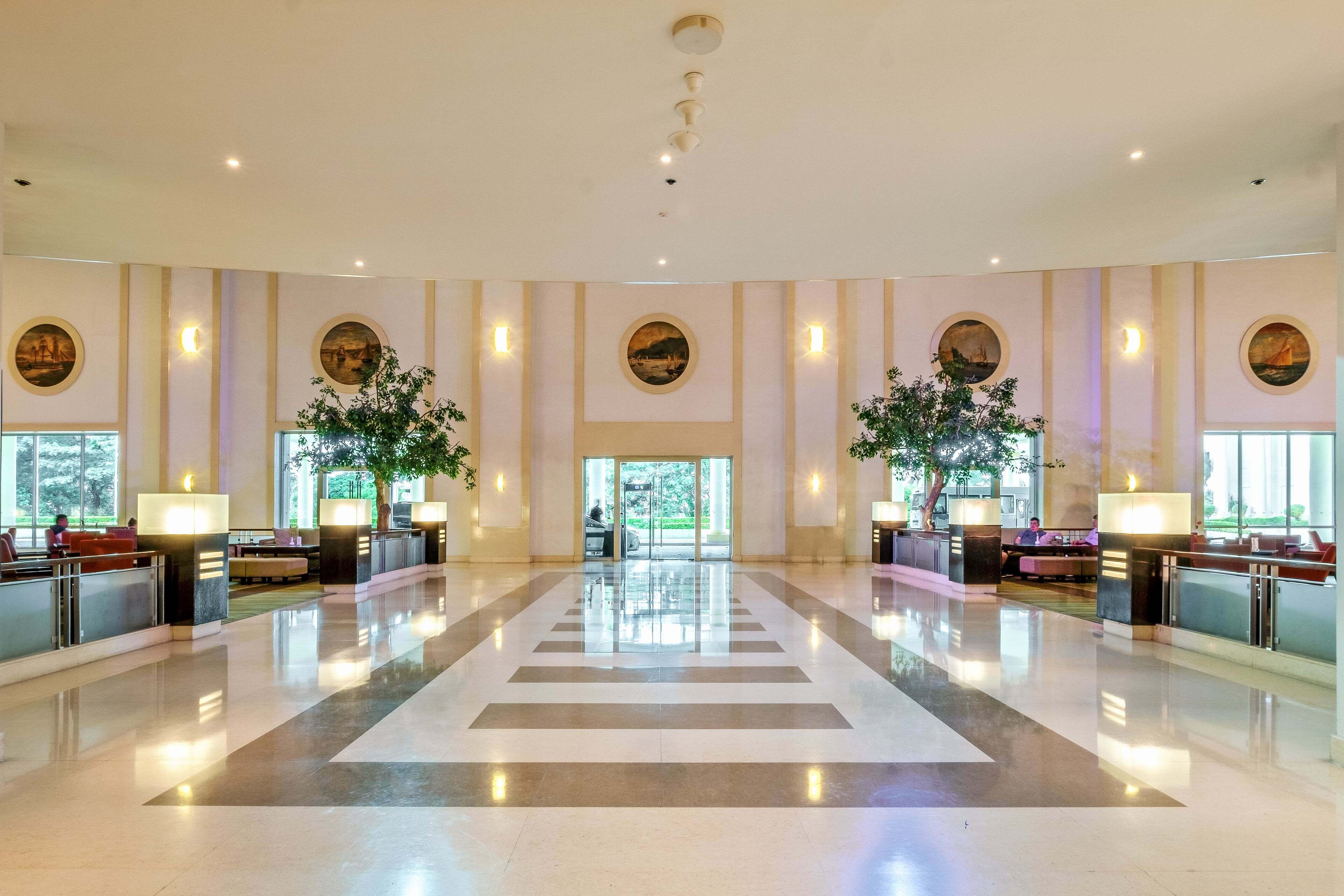 A spacious lobby with a central reflective floor, large windows, and wall-mounted lamps.