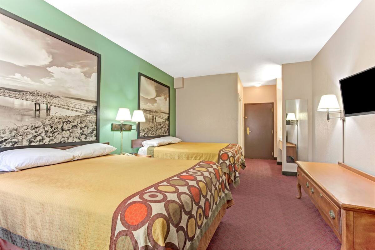 Une chambre d’hôtel avec deux lits, un grand tableau au mur, une télévision et un bureau avec une lampe.