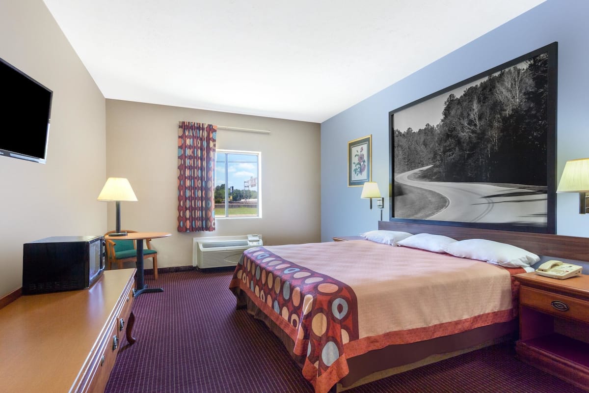 Une chambre d’hôtel avec un lit, un bureau doté d’une lampe, une télévision et une grande fenêtre avec des rideaux.