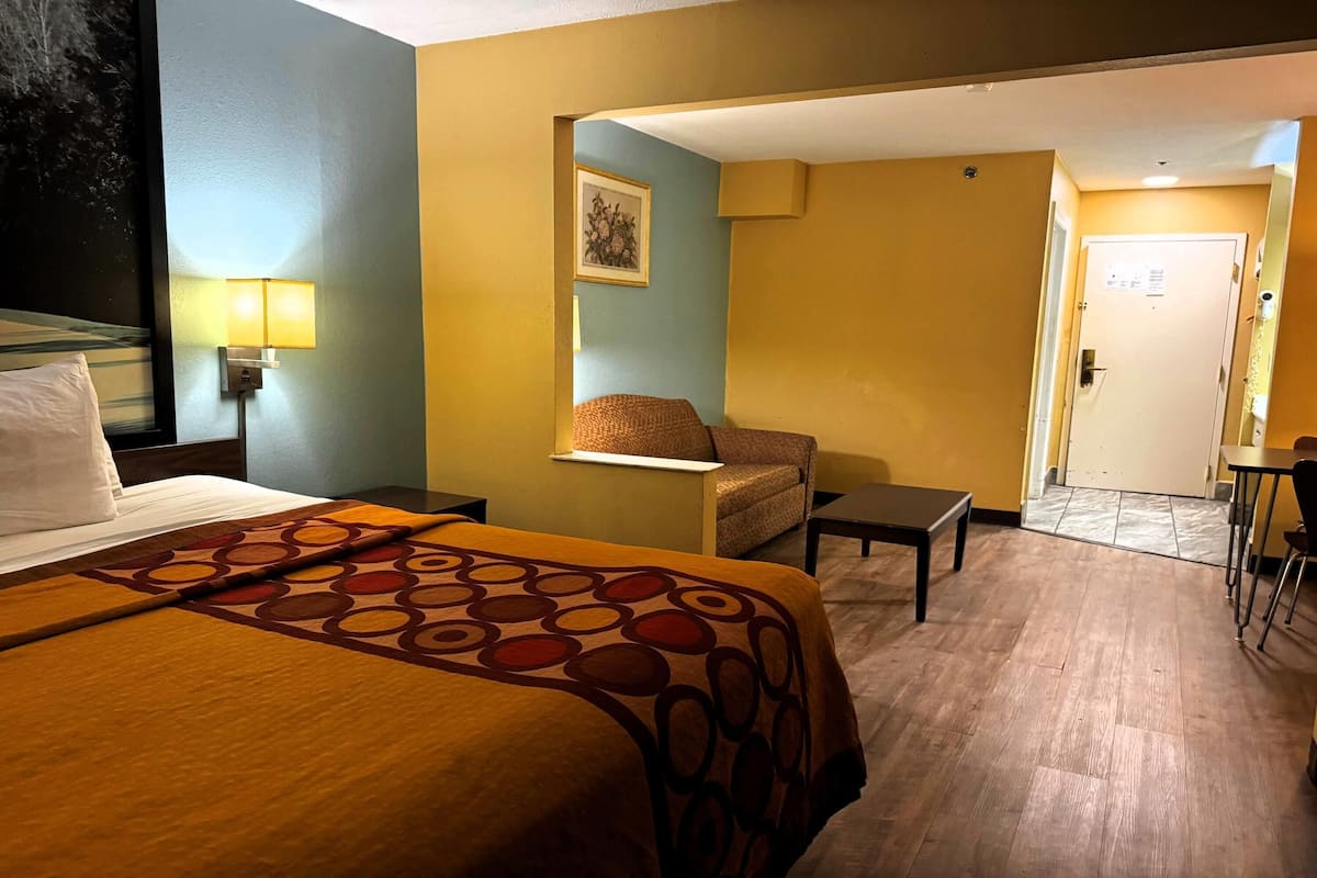 Une chambre d’hôtel avec un grand lit, une chaise, une petite table et une porte donnant sur une autre pièce.