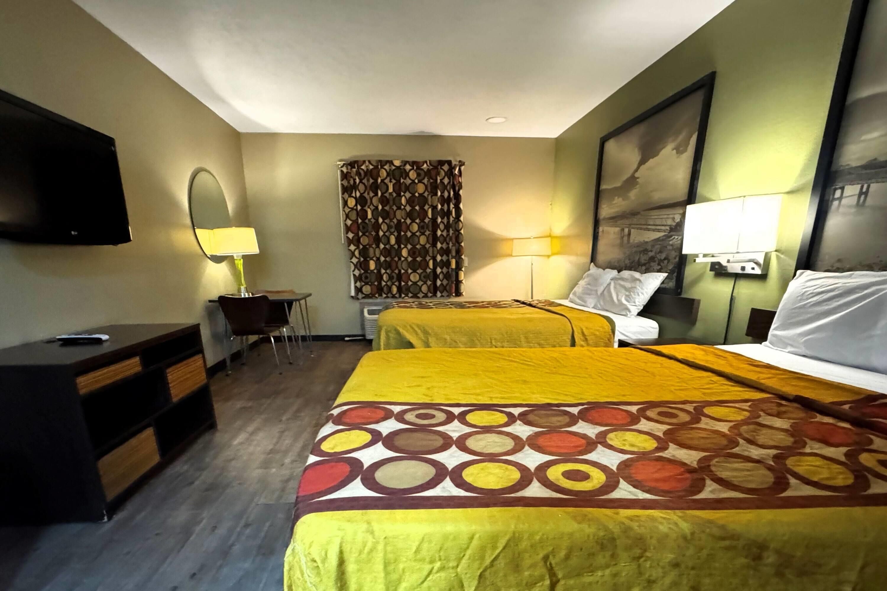 A hotel room with two beds, a desk, a chair, a TV, and a window with curtains.