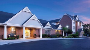A row of modern, two-story residential buildings with brick facades and white trim, featuring a central entrance with a bench and potted plants. - Residence Inn by Marriott Kansas City Overland Park (Overland Park)