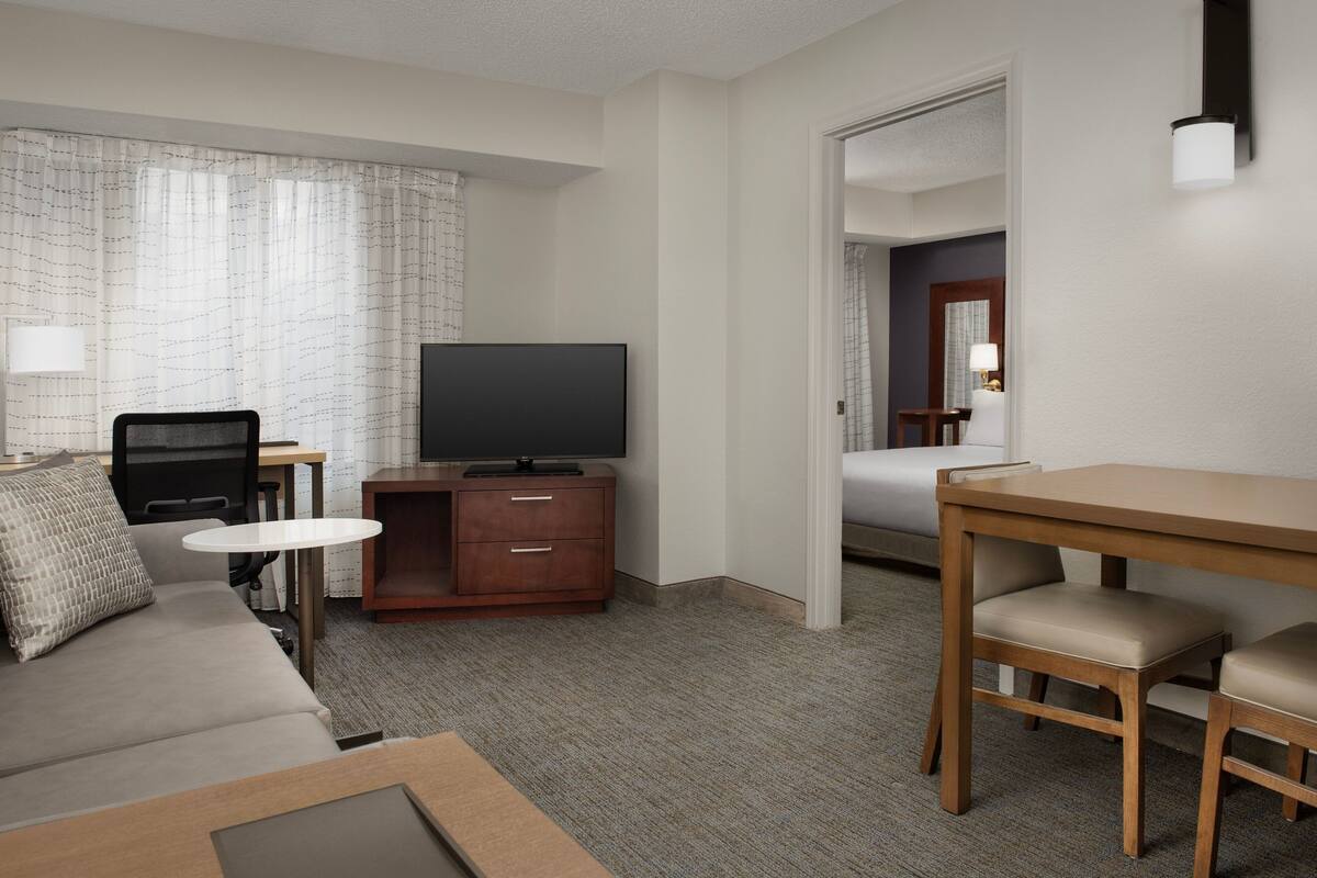 A hotel room with a flat-screen TV, a sofa, a small table, a desk with two chairs, and a bed.