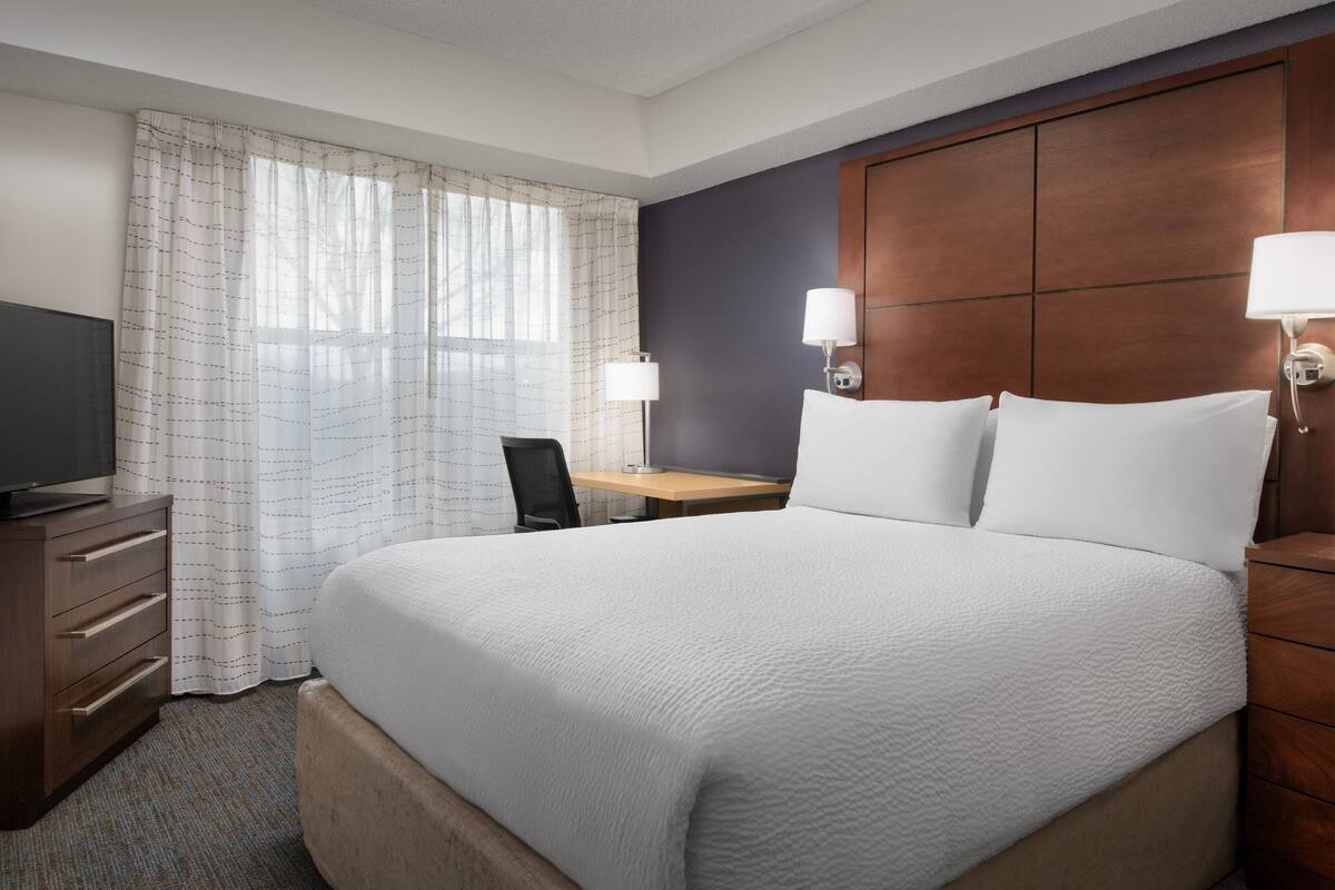 A hotel room with a large bed, a desk, a chair, and a television.