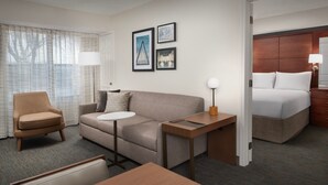 A hotel room with a sofa, armchair, small round table, and a bed with a wooden headboard. There are three framed pictures on the wall. - Residence Inn by Marriott Kansas City Overland Park (Overland Park)