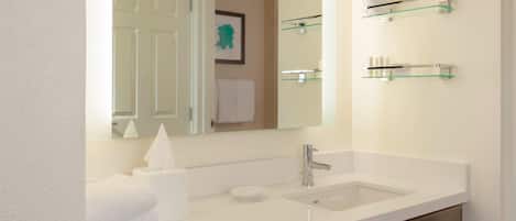 A modern bathroom with a white sink, a mirror, and glass shelves above the sink.