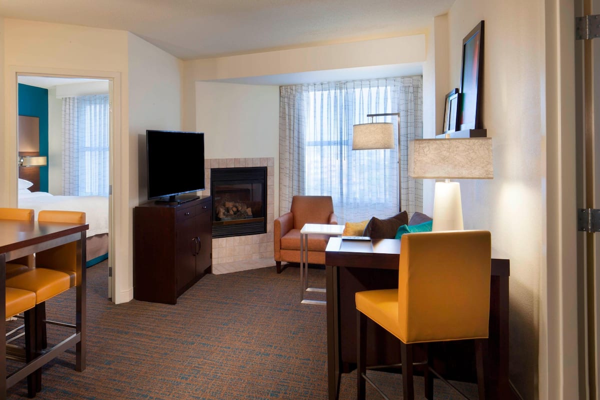 Habitación de hotel con televisor, chimenea, comedor y vista panorámica de la ciudad a través de amplios ventanales.