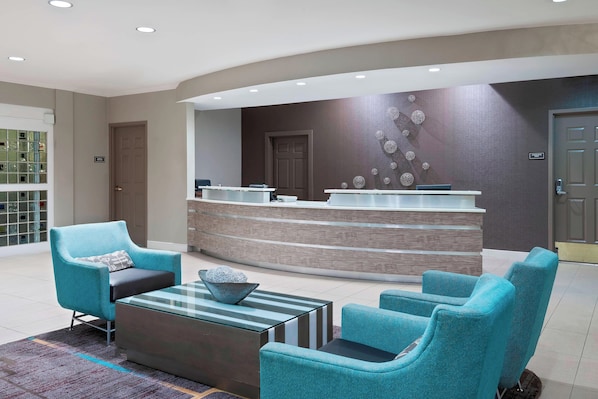 A modern reception area with a curved reception desk, teal armchairs, and a glass coffee table.