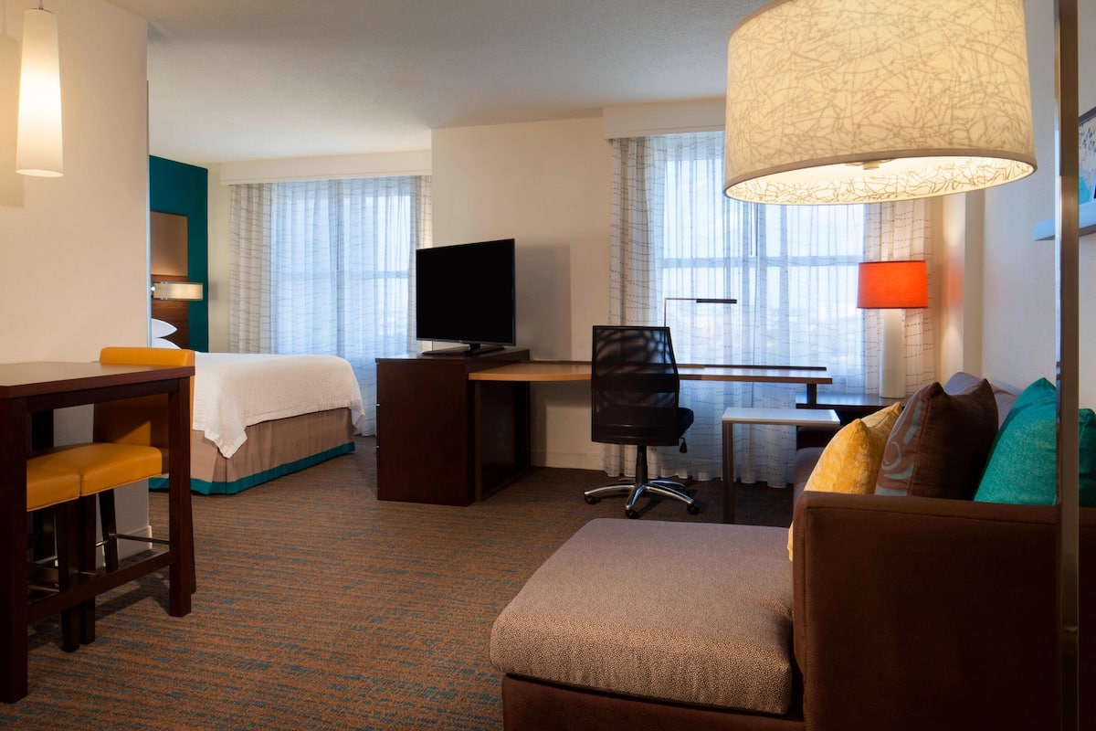 Habitación de hotel con cama, escritorio, silla, televisor y sofá.