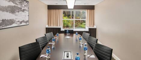 A conference room with a long table, black chairs, water bottles, and a large window with curtains.