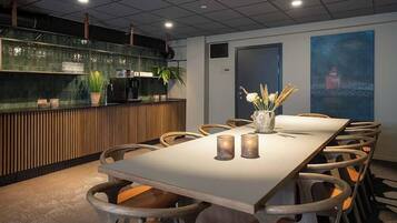 Una sala conferenze con un lungo tavolo, sedie in legno, una parete divisoria in vetro con piante e un quadro appeso al muro.