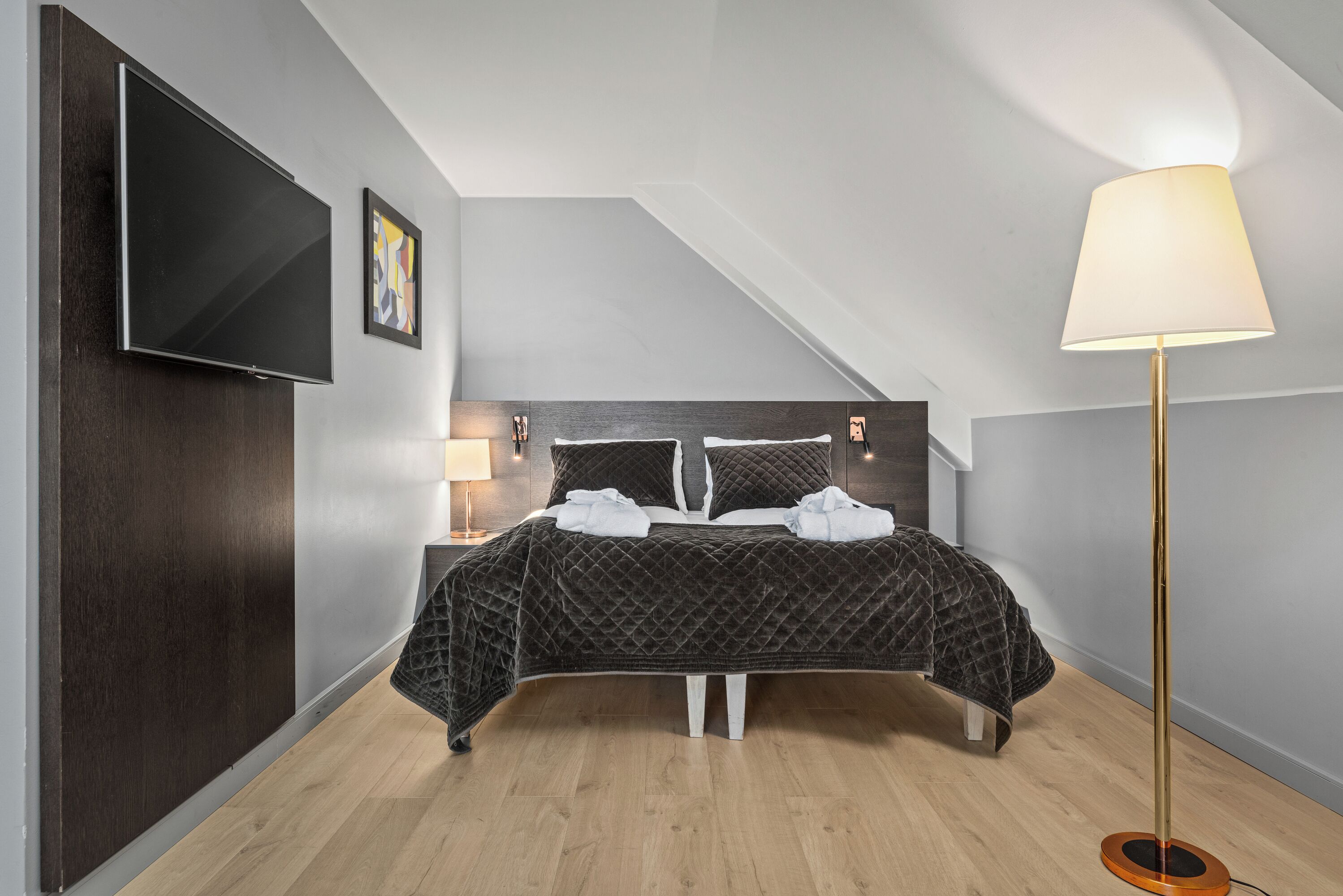 Une chambre à coucher moderne avec un lit, un téléviseur fixé au mur, une lampe sur pied et un cadre photo.
