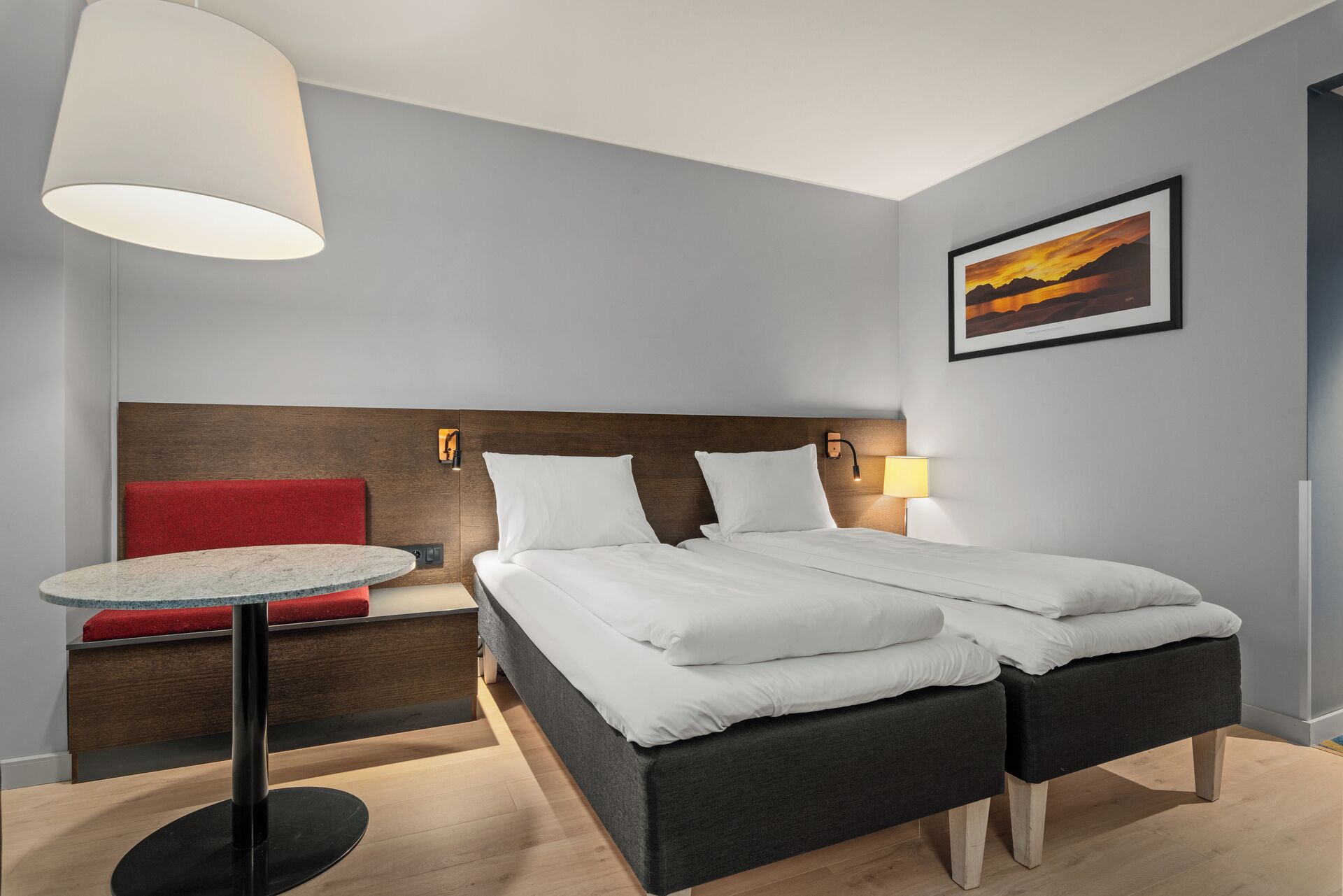 A modern hotel room with a bed, bedside table, lamp, and a painting on the wall.