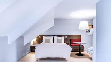Een moderne hotelkamer met een groot bed, een klein rond tafeltje, een rode stoel en een opvallend plafondontwerp.