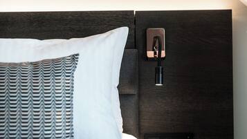 A modern hotel room with a neatly made bed, a nightstand with a lamp, and a wall-mounted charging station.