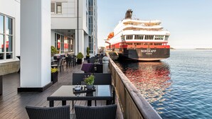 A waterfront restaurant with outdoor seating overlooking a large cruise ship docked at the pier.