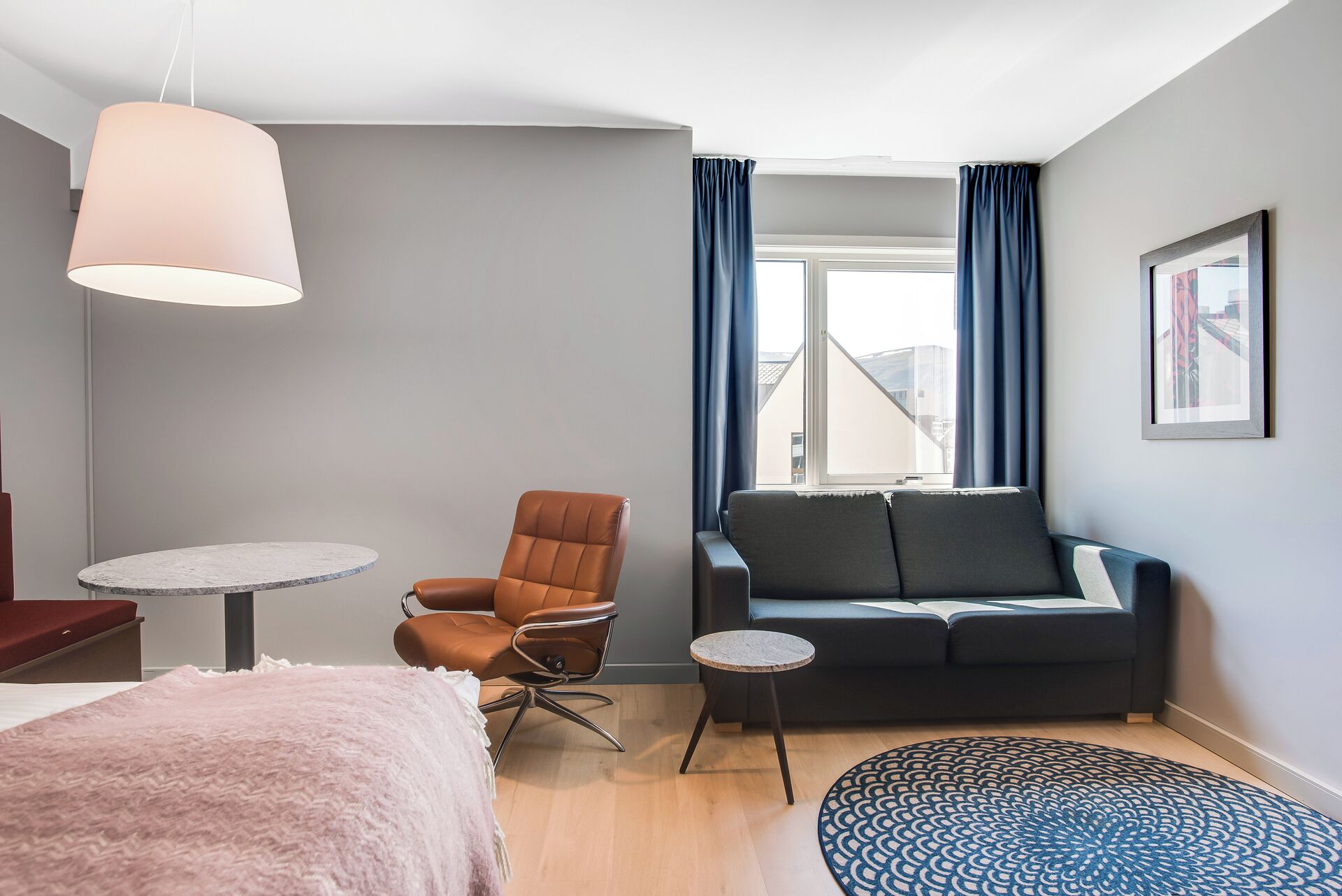 A modern hotel room with a bed, a sofa, a chair, a small table, and a large window with curtains.