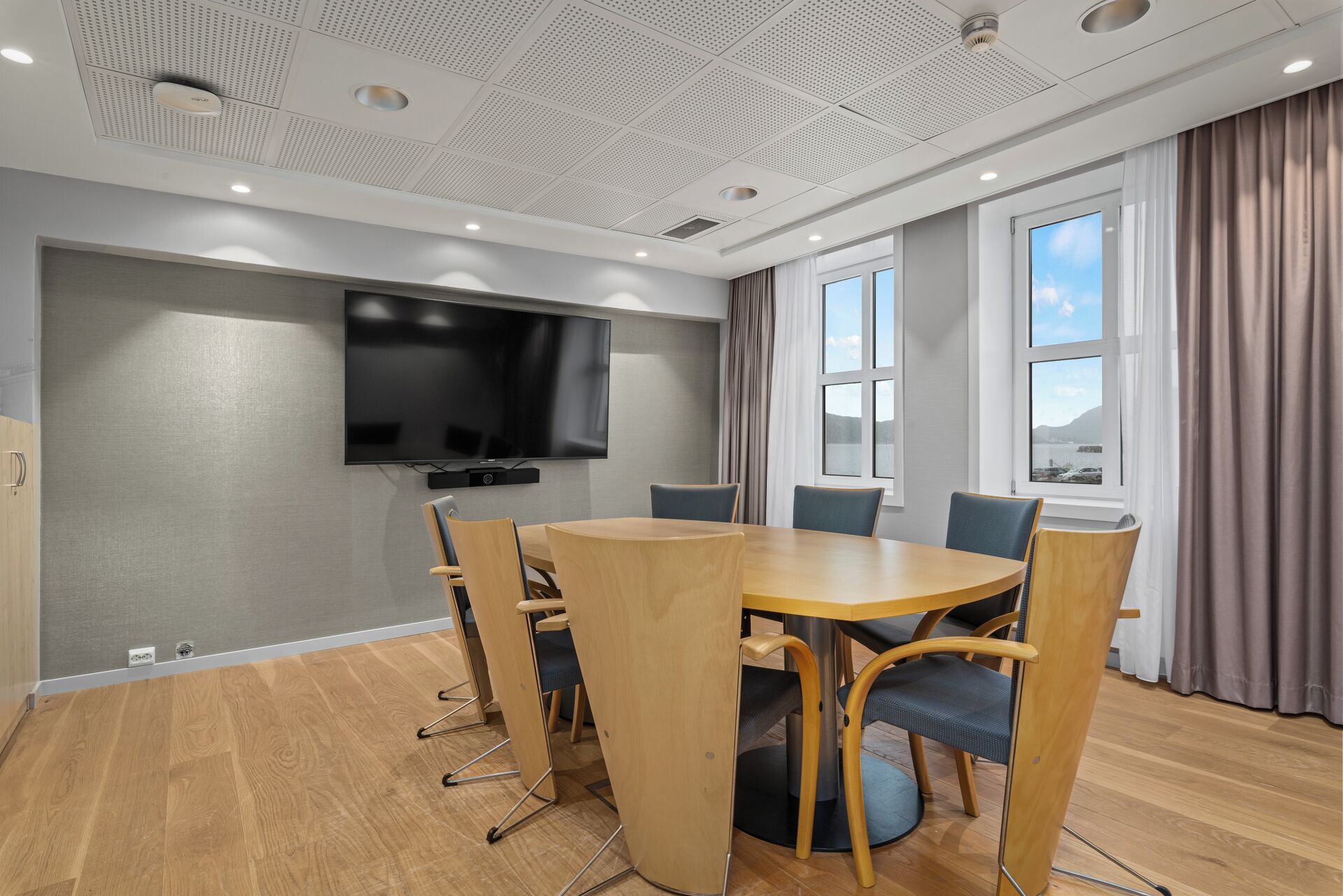 Una sala conferenze con una grande TV a schermo piatto, un tavolo rotondo in legno e sei sedie.