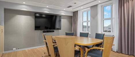 A conference room with a large flat-screen TV, a round wooden table, and six chairs.