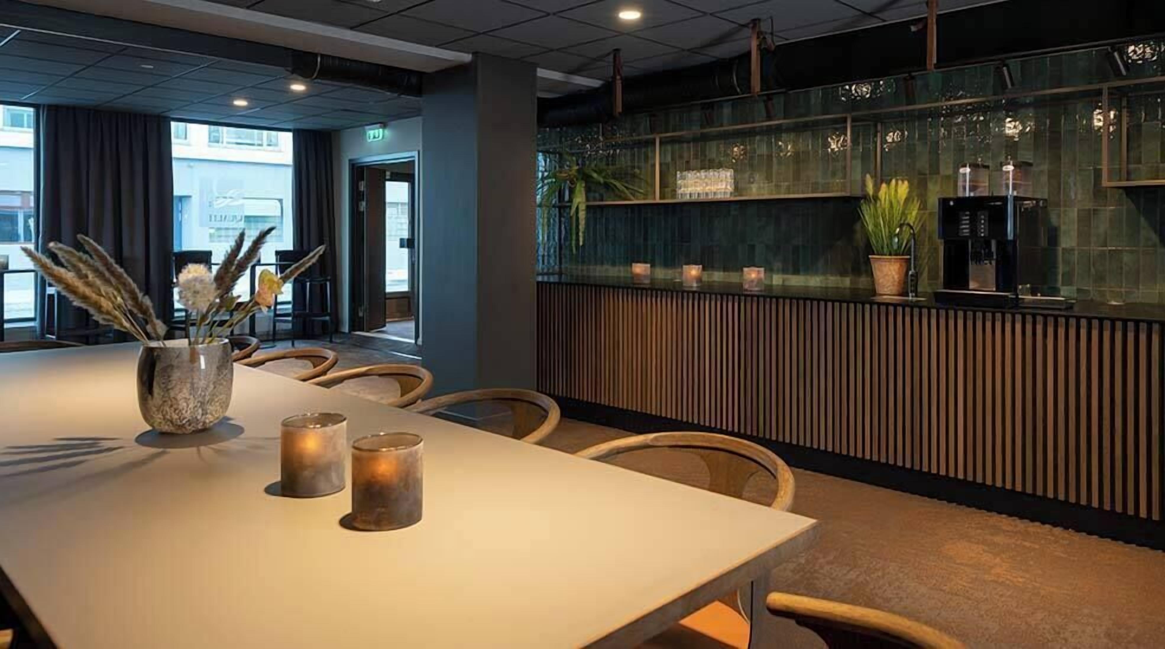 A modern conference room with a long table, chairs, and a decorative vase with dried plants.