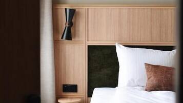 Una habitación de hotel con cabecera de madera, una mesita de noche con lámpara y cama con ropa blanca.