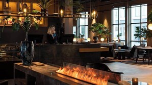A modern bar area with a central fire feature, wooden furniture, and potted plants.