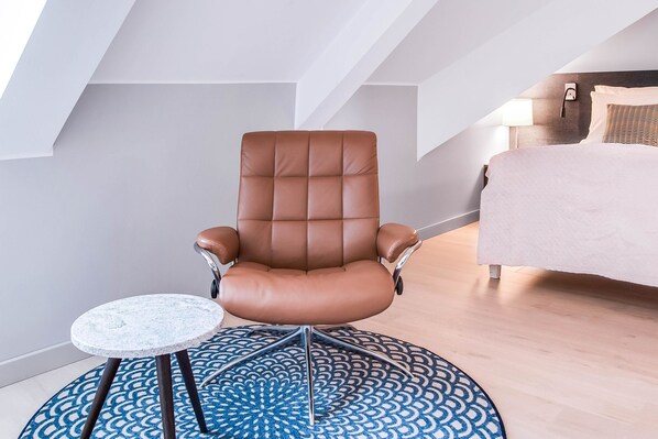 Una habitación moderna con un sillón de cuero marrón, una mesita redonda pequeña y una alfombra estampada.