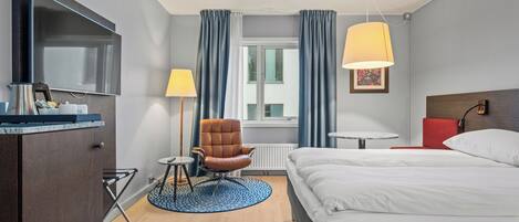 A hotel room with a bed, a chair, a desk, a lamp, and a TV.