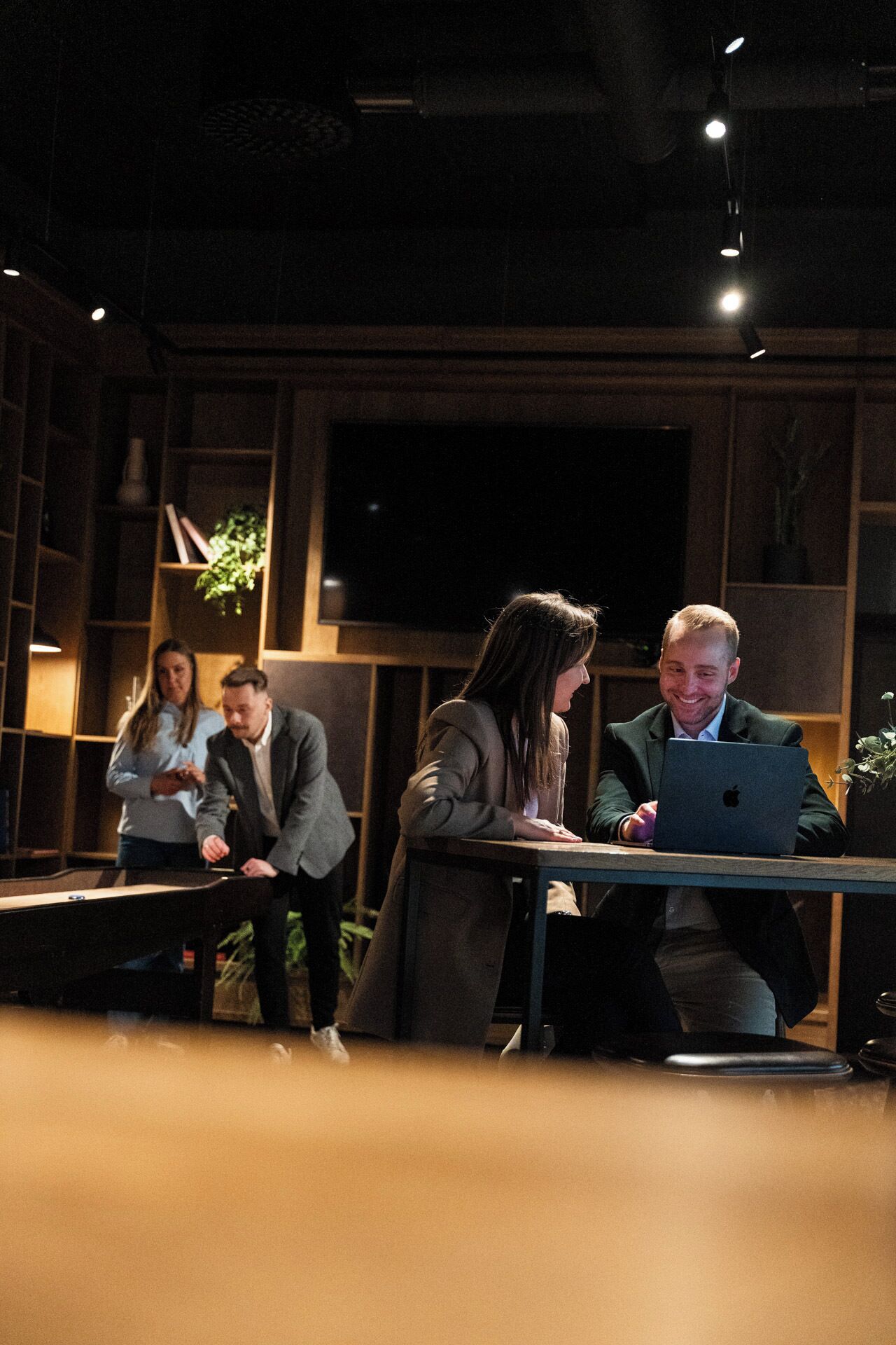 A group of people in a dimly lit room with wooden paneling and a large flat-screen TV mounted on the wall.