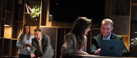 A group of people in a dimly lit room with wooden paneling and a large flat-screen TV mounted on the wall.