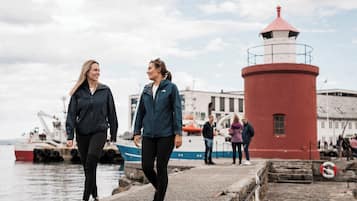 Two people walking on a pier with a red lighthouse in the background.