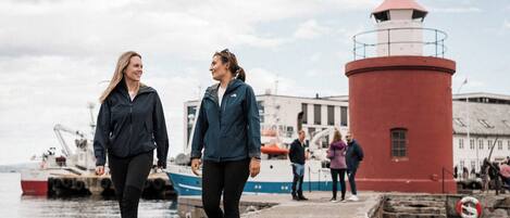 Two people walking on a pier with a red lighthouse in the background.