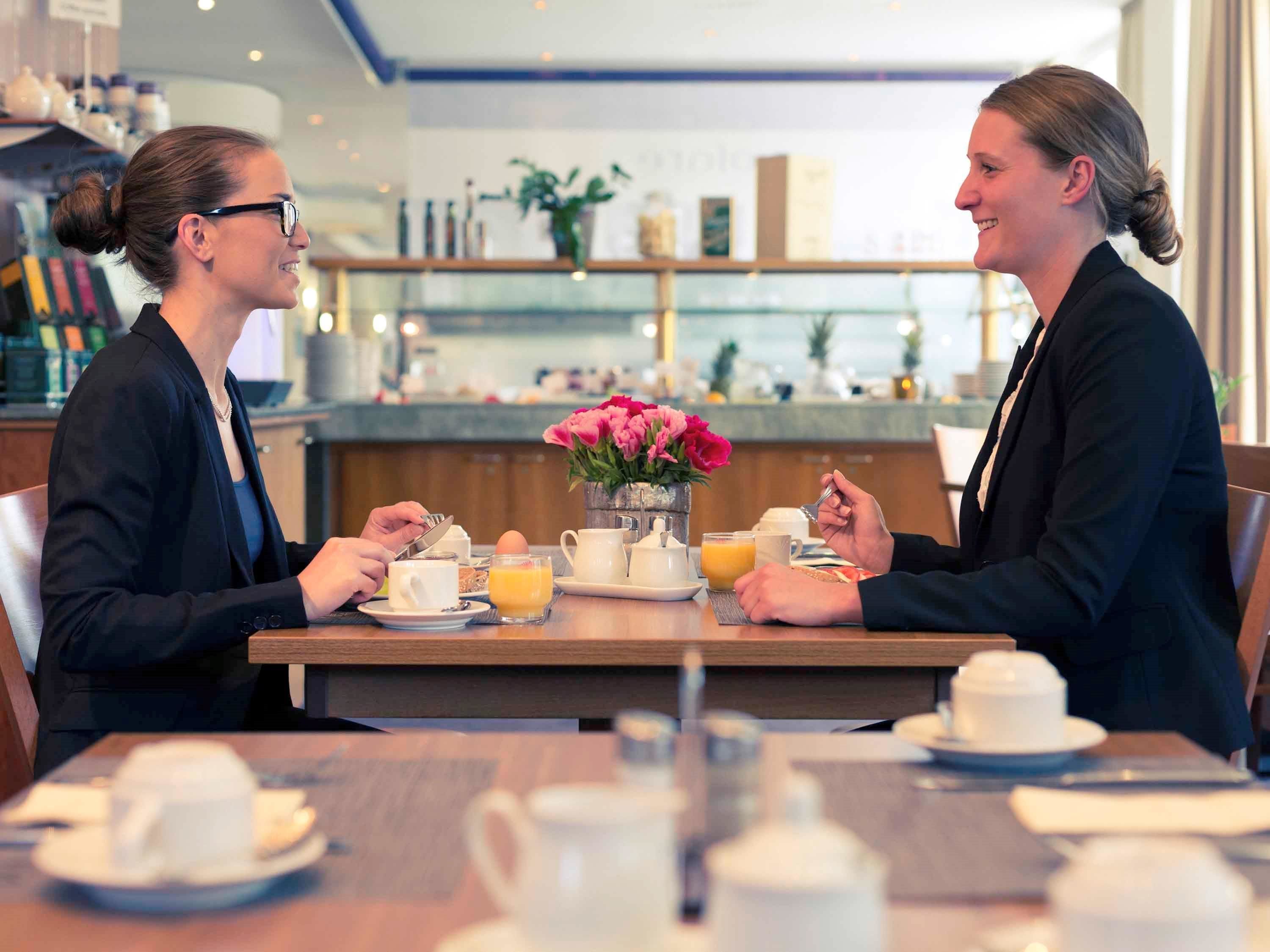 Dos personas sentadas a la mesa del desayuno con café, té y zumo de naranja.