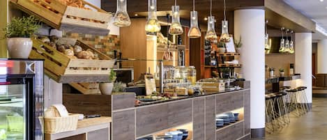 Interior moderno de una cafetería con mostrador de madera, luces colgantes y una variedad de productos alimenticios a la vista.