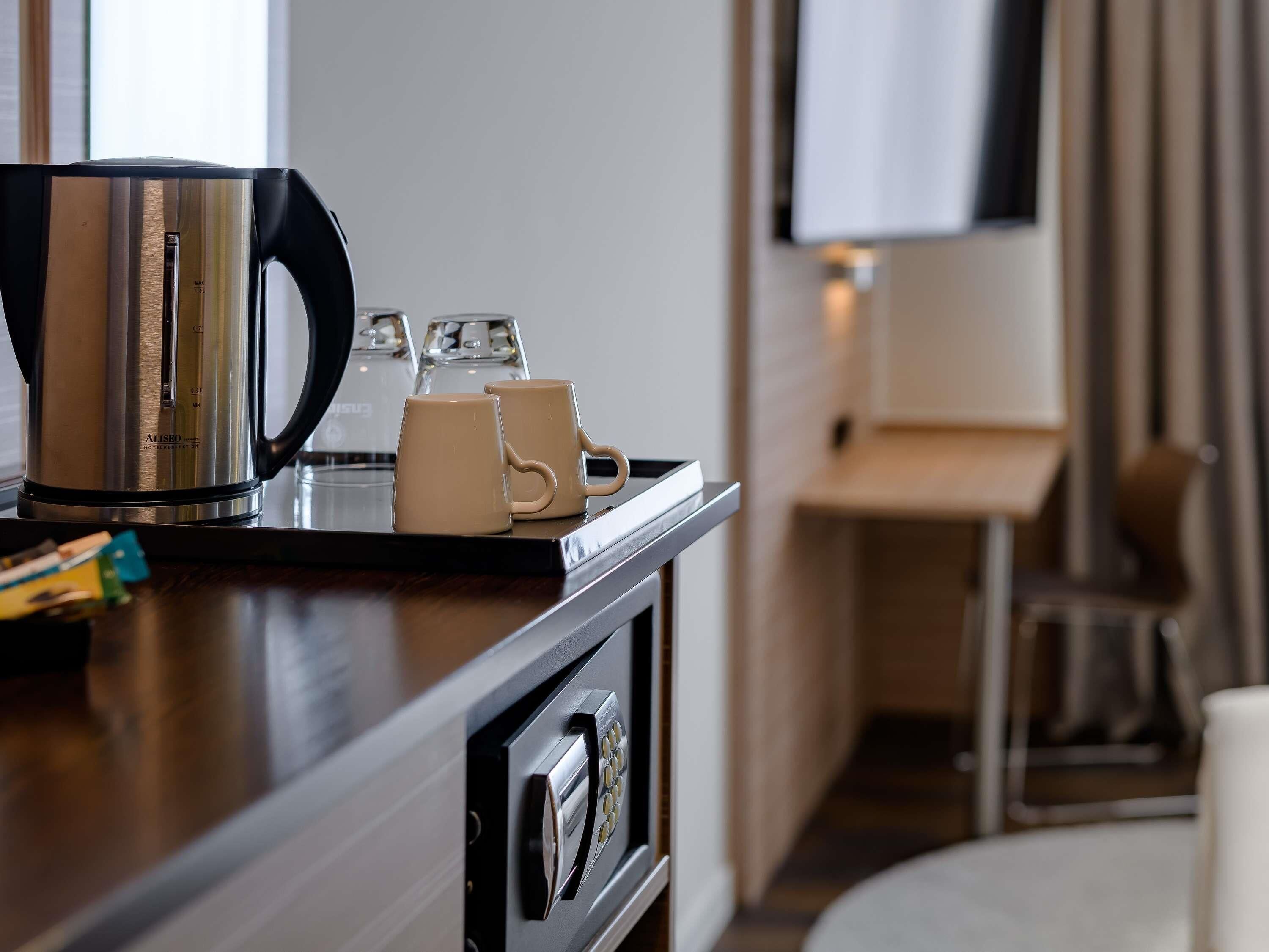 A hotel room with a coffee maker, two mugs, and a tray on the counter.