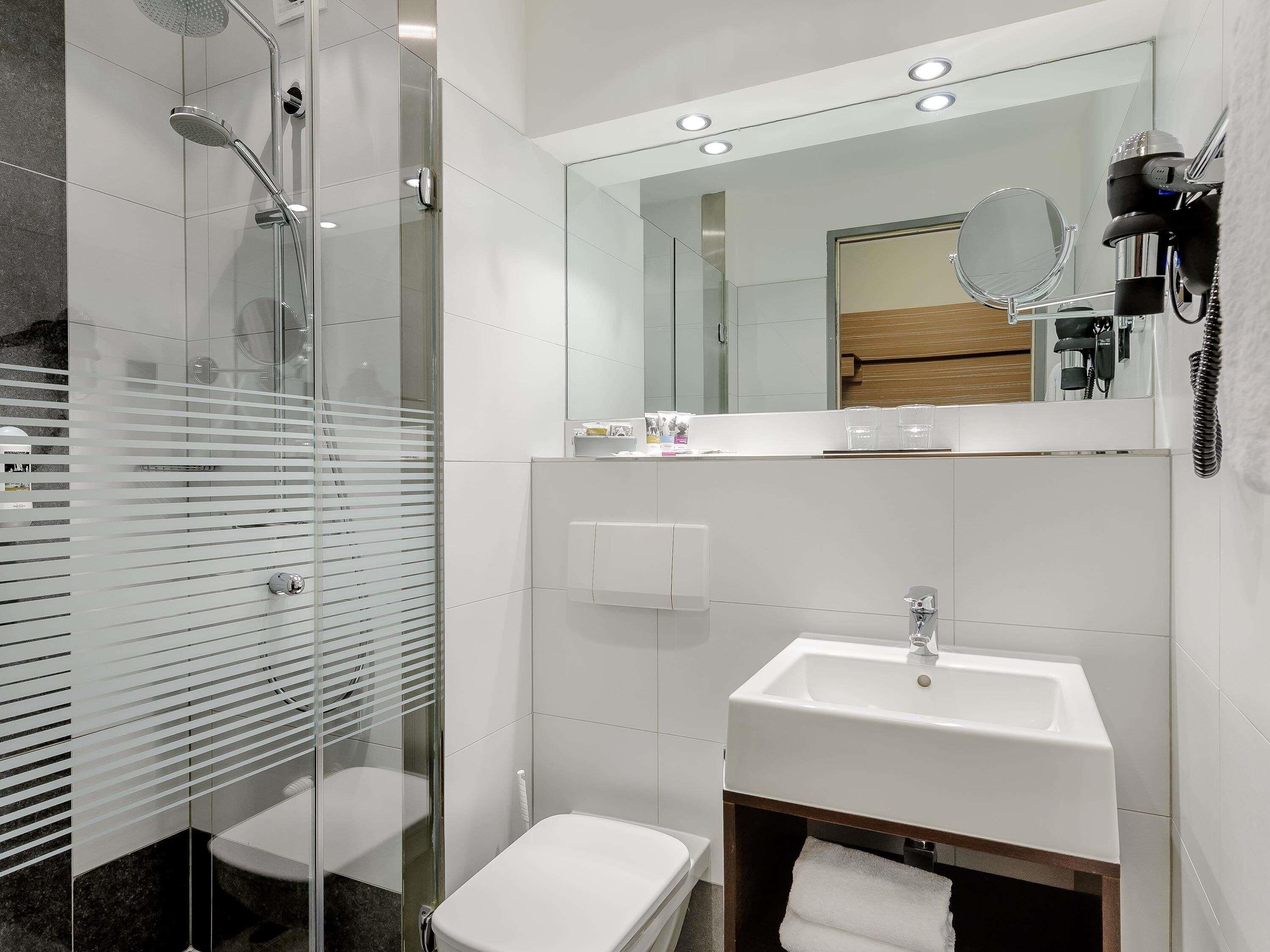 A modern bathroom with a glass-enclosed shower, a white sink, and a mirror above the sink.
