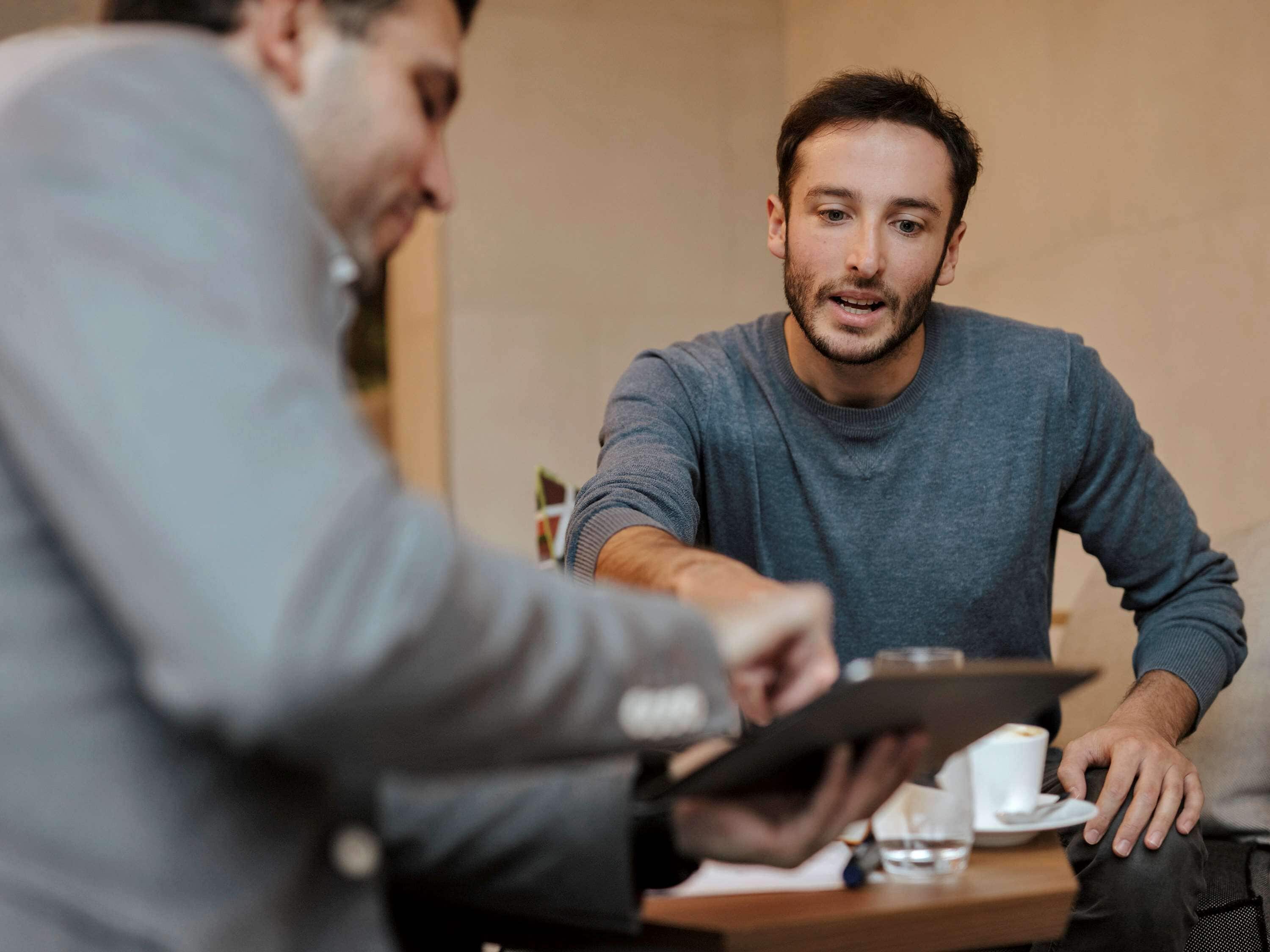 Dos personas sentadas en una mesa con una tableta y una taza de café.