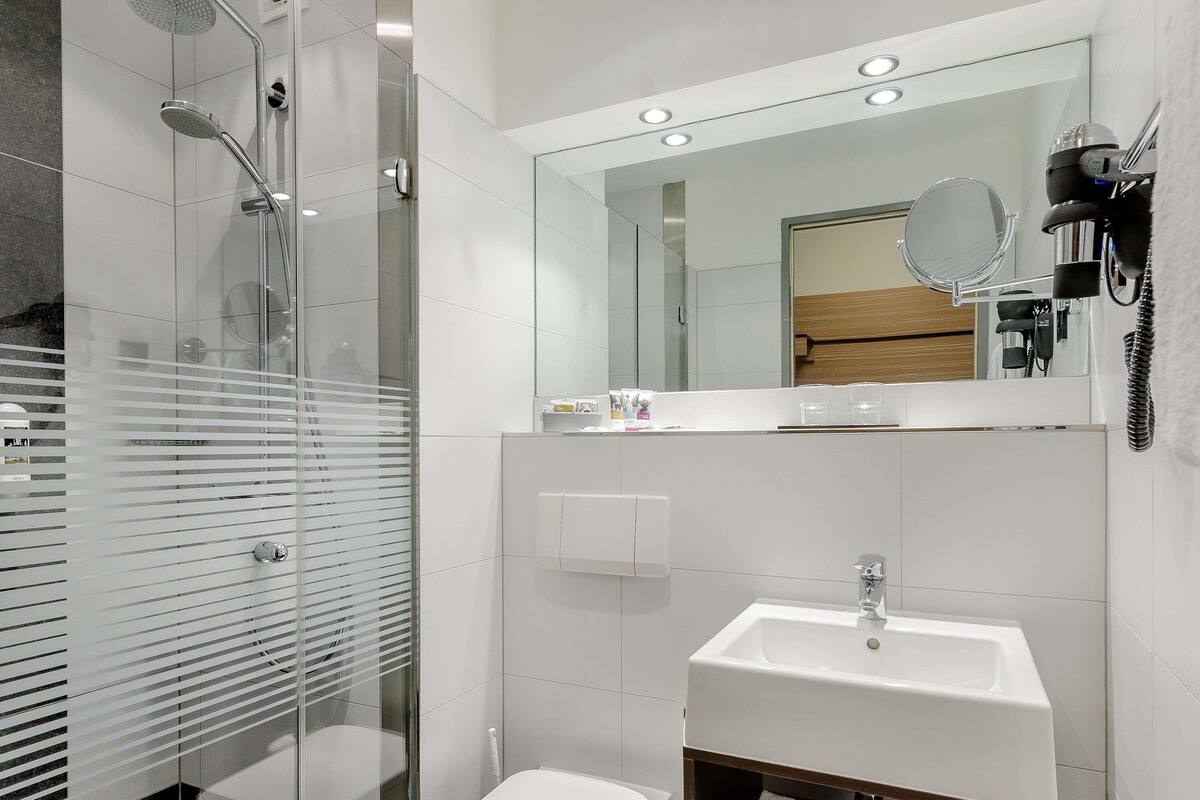 Une salle de bain moderne avec une douche en verre, un lavabo blanc et un miroir au-dessus du lavabo.