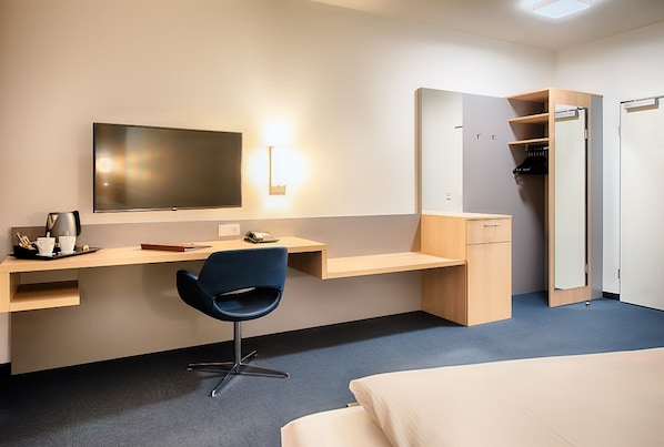 Una habitación de hotel con cama, escritorio con silla, televisión, armario y espejo.