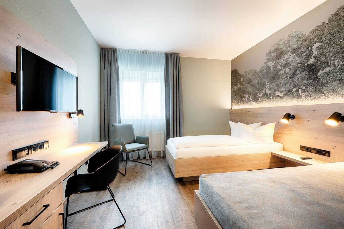 A modern hotel room with a wooden desk, a bed, a chair, and a large TV.