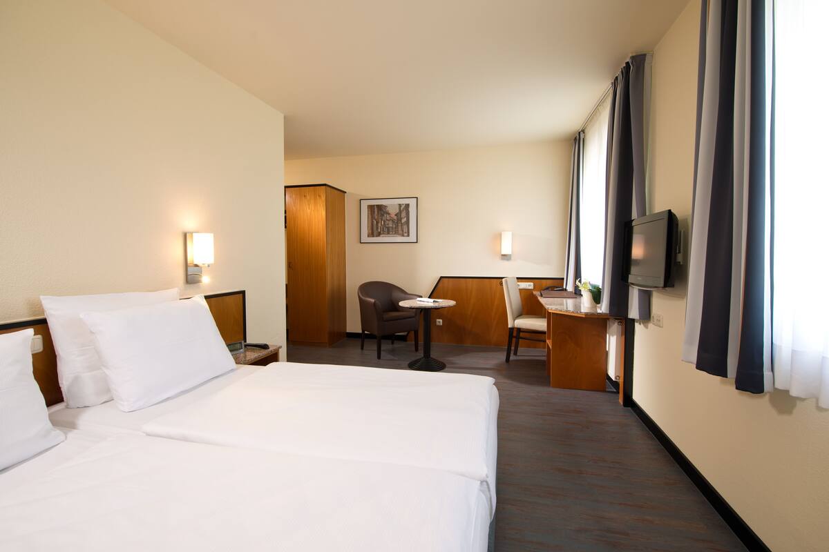 A hotel room with a large bed, a desk, a chair, a small table, and a television.