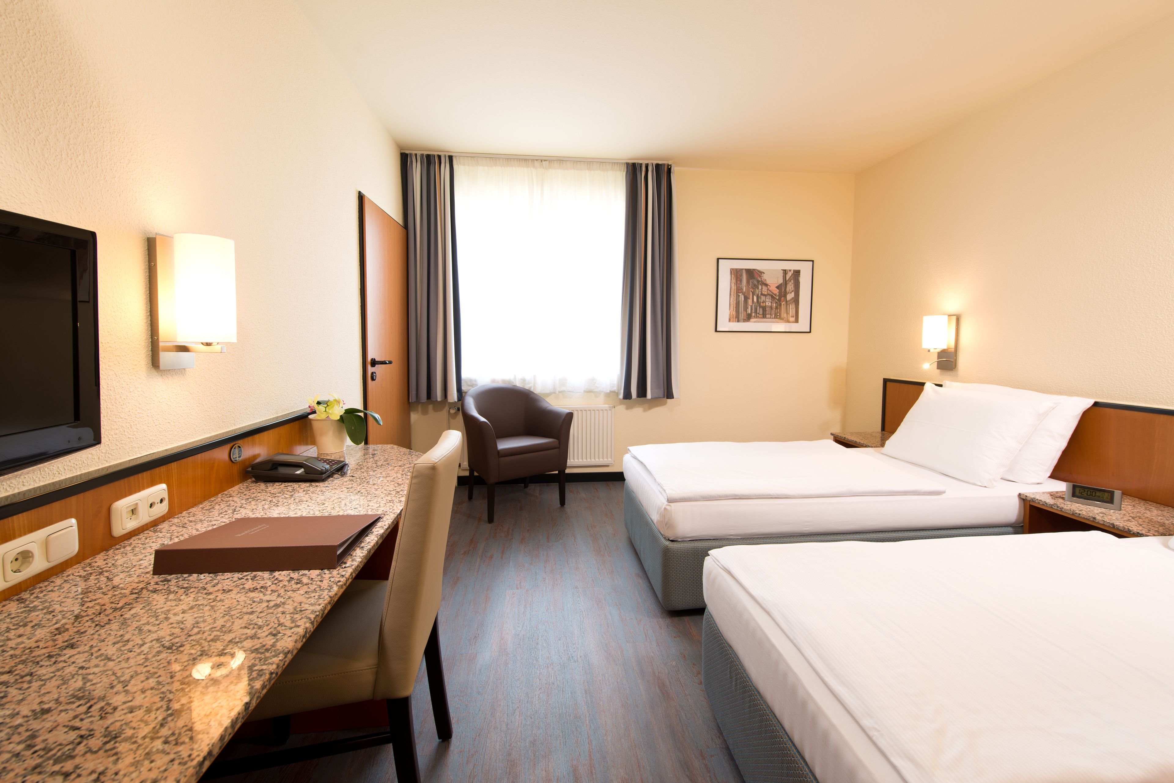 A hotel room with a bed, a desk, a chair, a TV, and a window with curtains.